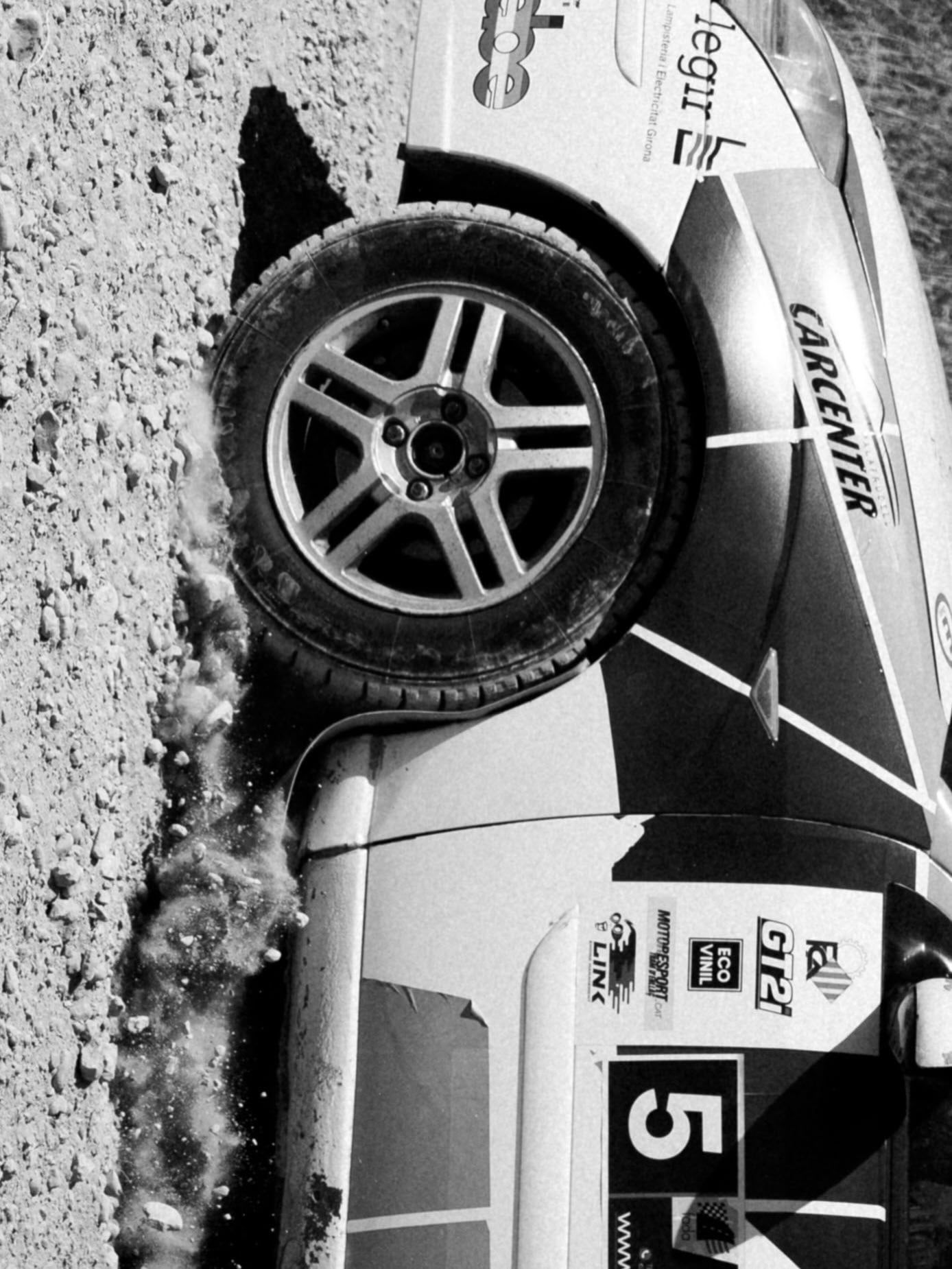 Rueda delantera de un coche de rally en un talud, en blanco y negro